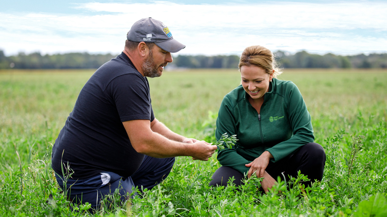An agri-advisor and a farmer crouched in a cover crop field.