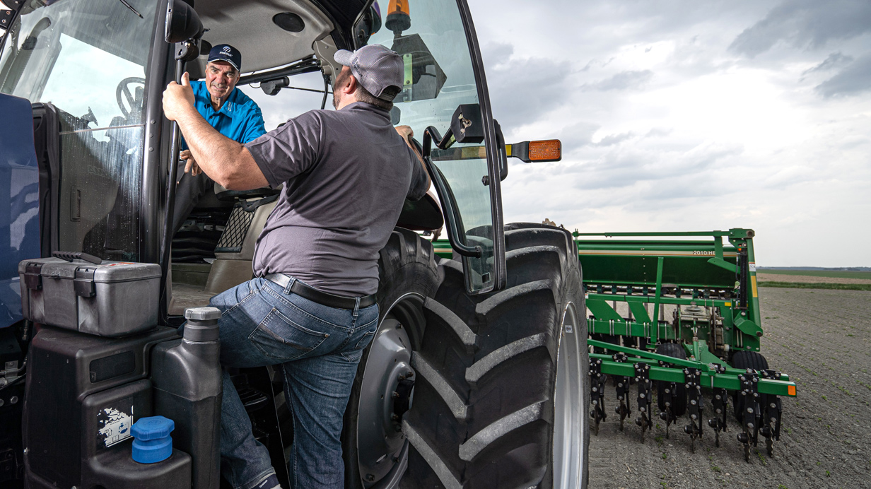 An agri-advisor and a farmer chat in a tractor while planting corn.