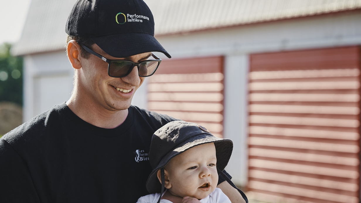 The winner of a Dairy Performance Award poses in front of his farm with his baby.